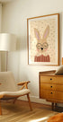 ein gemütliches Wohnzimmer mit einem beigen Sessel, einer Holzkommode und einem gerahmten Bild eines Hasen mit Brille.