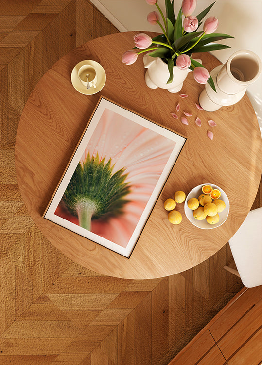 ein Holztisch mit einem gerahmten Bild einer Blume, einer Obstschale und einer Vase mit rosa Blumen.