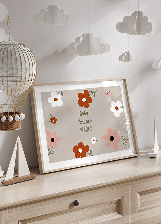 Auf einer Holzkommode ist ein gerahmter Druck mit Blumenmuster und dem Text „Baby You are Magic“ zu sehen, darüber hängt eine dekorative Papierlaterne.