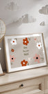 Auf einer Holzkommode ist ein gerahmter Druck mit Blumenmuster und dem Text „Baby You are Magic“ zu sehen, darüber hängt eine dekorative Papierlaterne.